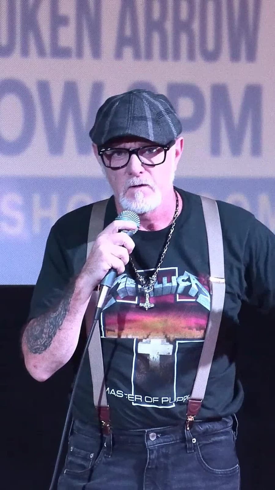 Uncle Danny performing with a microphone, flat cap, glasses, and suspenders